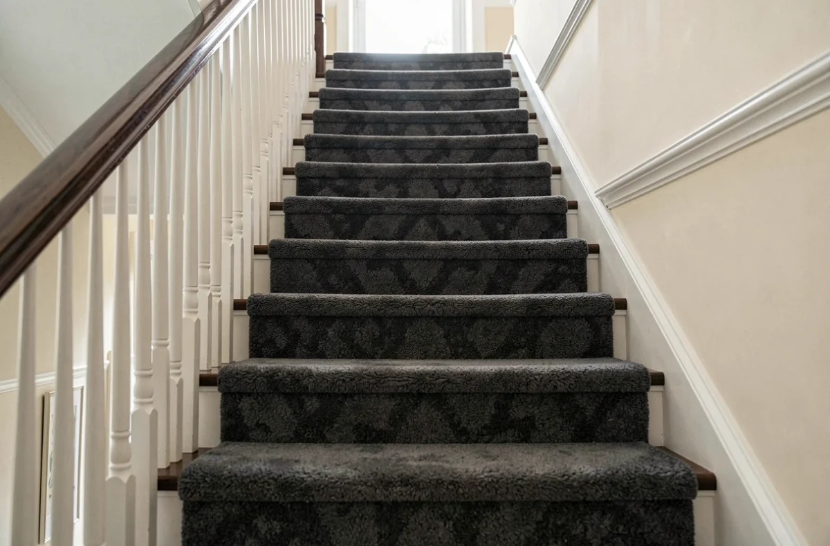 Vue d'ensemble d'un escalier résidentiel entièrement recouvert de marches en moquette gris anthracite posées régulièrement, depuis le bas de la montée