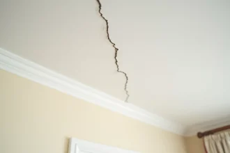 Fissure fine et diagonale sur un plafond en plâtre blanc d'un appartement ancien, vue en gros plan montrant les détails de la cassure