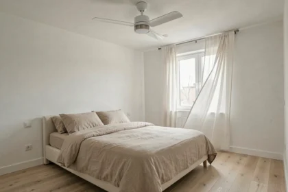 Ventilateur de plafond silencieux blanc au-dessus d'un lit dans une chambre minimaliste scandinave avec parquet en chêne et rideaux en lin